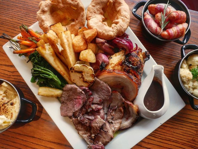 Overhead view of a sharing platter of roast meats with Yorkshire puddings, roast vegetables and a jug of gravy.