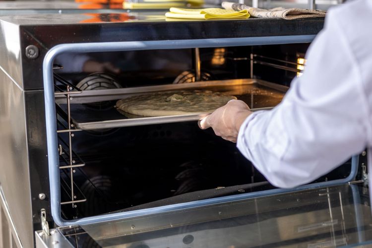 A chef in whites using a peel to slide a pizza into a stainless commercial oven.