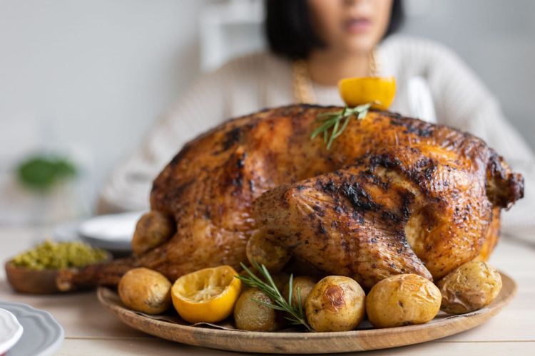 A golden roasted turkey resting on a wooden platter with lemons, new potatoes and rosemary