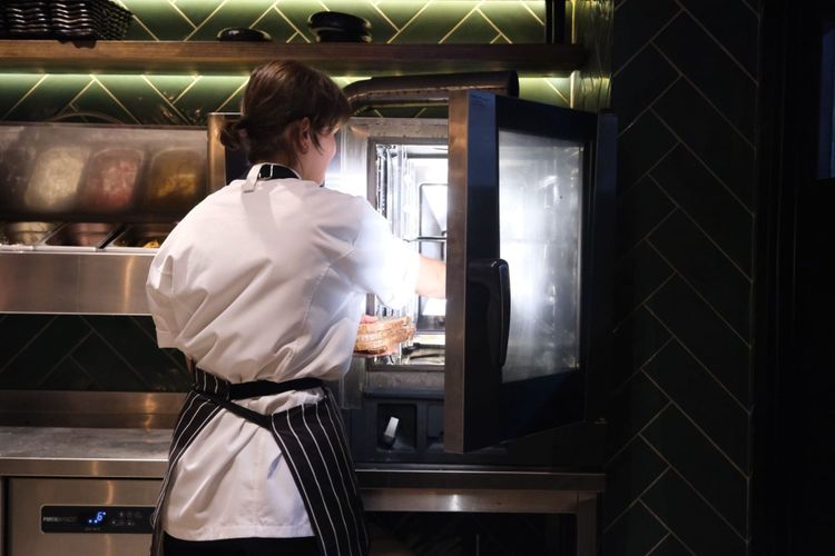A chef loading a tray into a combination oven in a modern commercial kitchen