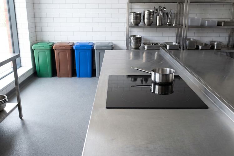 A commercial kitchen with an induction hob and four colour coded waste separation bins lined against the wall