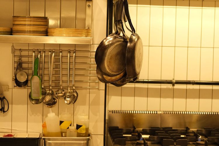 A commercial kitchen with gas ranges, hanging pans and shelves of stacked plates