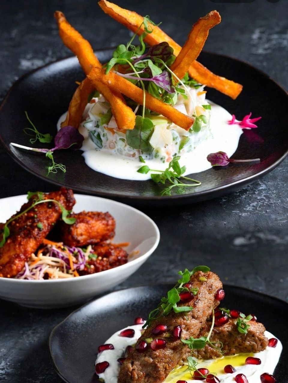 Small plates on a dark plate, crispy chicken bites with slaw and carrot sticks, finished with herbs and flowers.