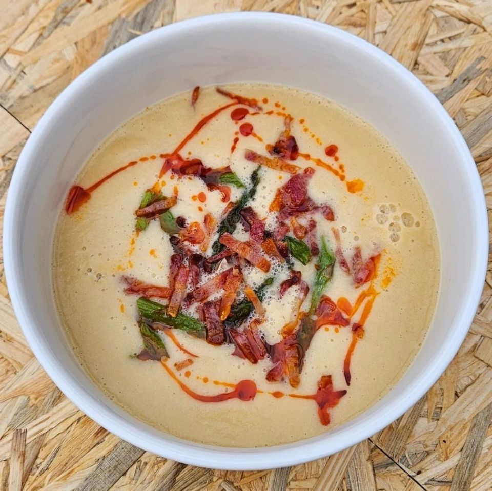 White bowl of creamy leek and butter bean soup topped with crispy chorizo, greens and chilli oil, seen from above.