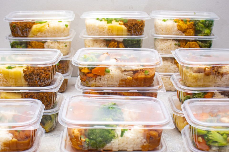 Rows of stacked clear takeaway containers filled with rice, chicken and vegetables.
