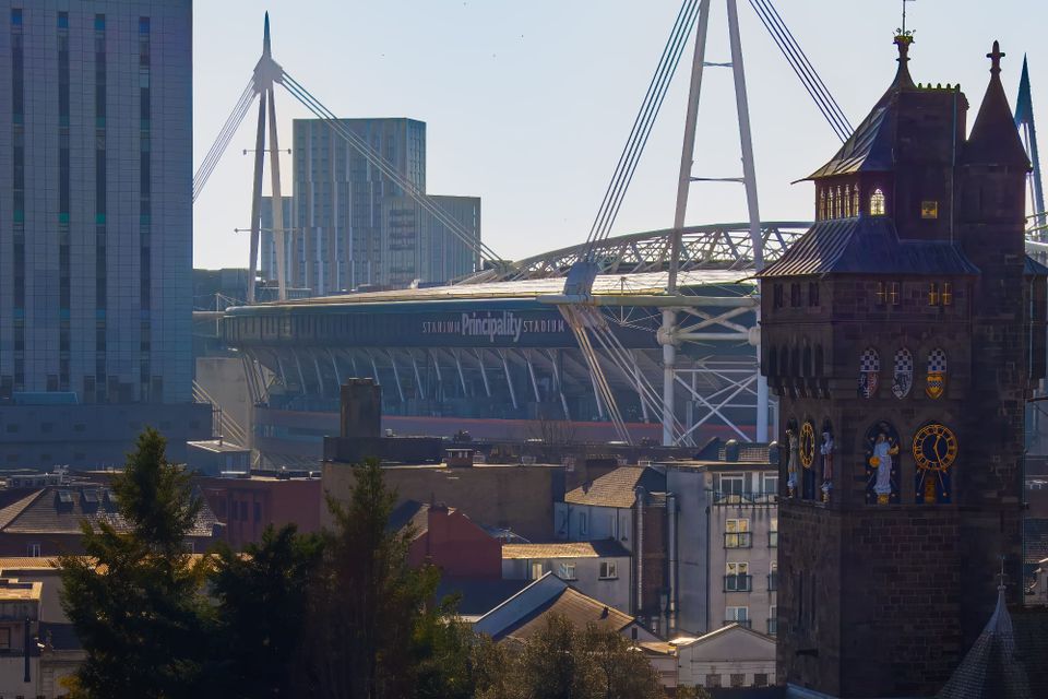 Cardiff Castle clock tower with the Principality Stadium and its roof masts rising behind city rooftops.
