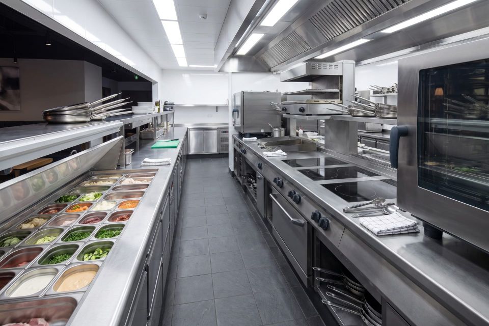 A commercial kitchen line set up and ready for service, prepped mise en place in gastronorms along the counter with induction hobs and combination ovens beyond
