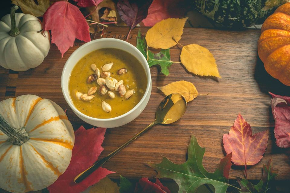 A bowl of pumpkin soup topped with toasted seeds, set among squashes and autumn leaves