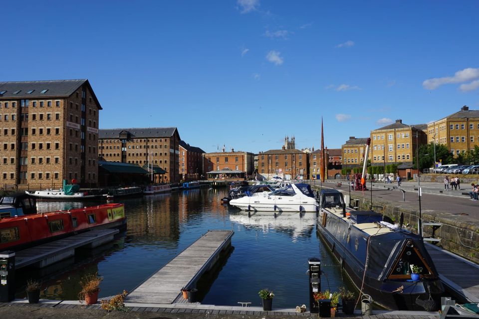 Brick warehouses around the main basin at Gloucester Docks with narrowboats and cruisers moored alongside.