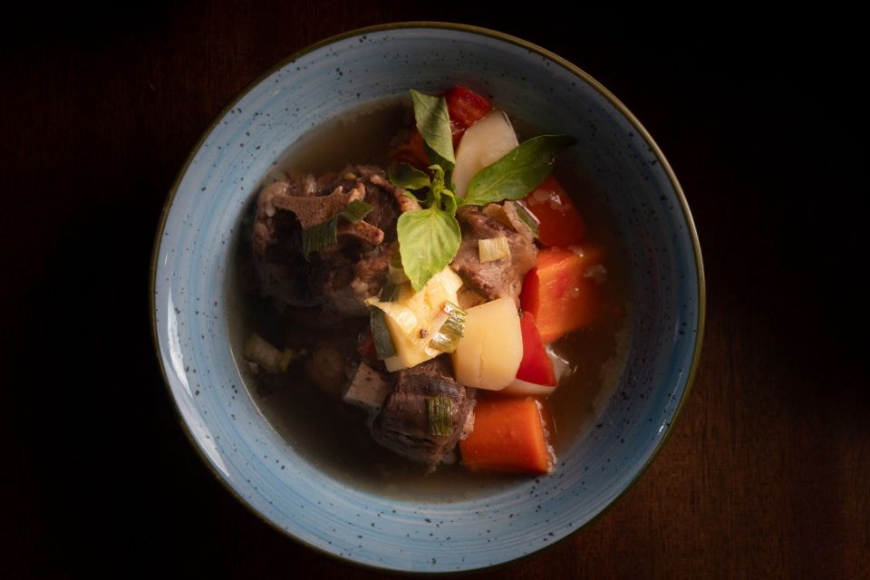 A dark bowl of slow cooked beef stew with root vegetables and fresh herbs