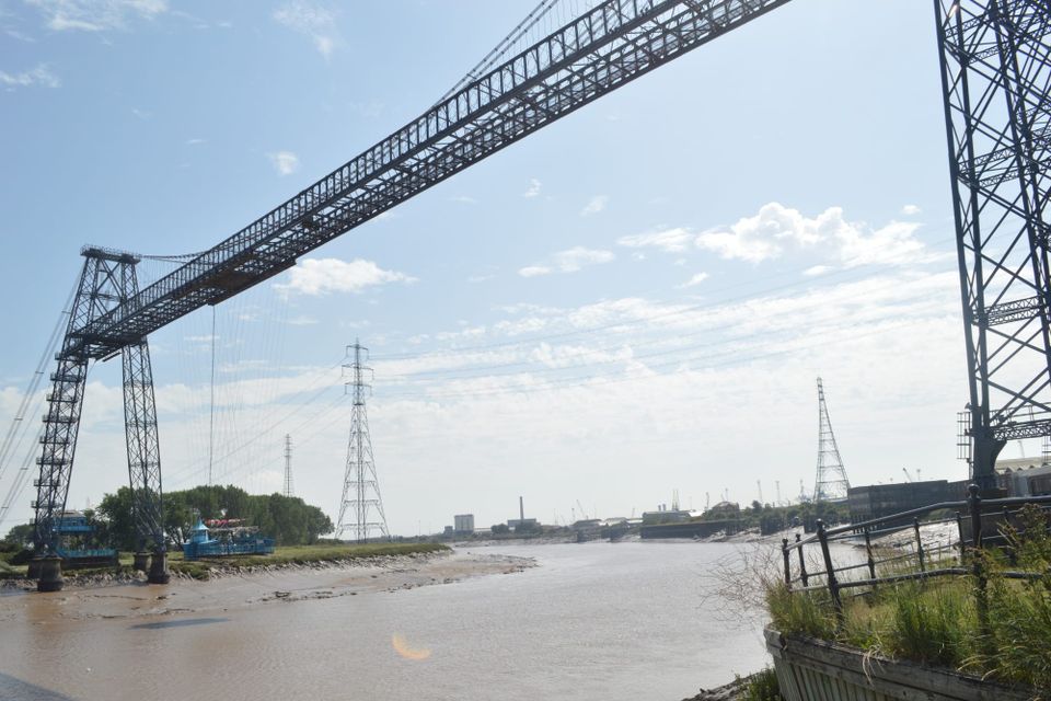 The Newport Transporter Bridge spanning the River Usk at low tide, seen from the bank above the mud flats.