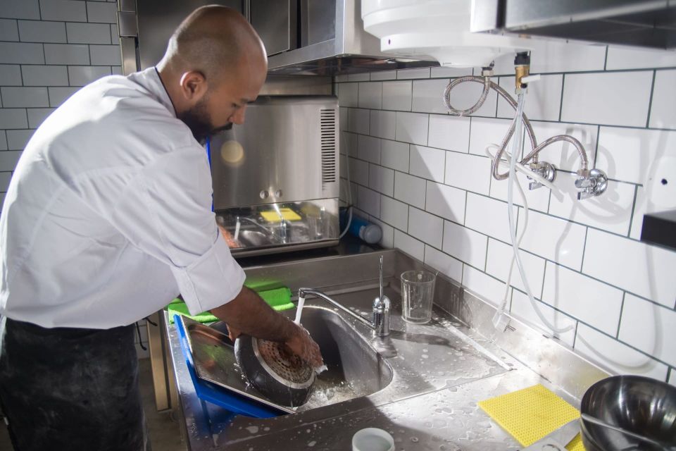 A chef washing up at the sink in a tiled commercial kitchen