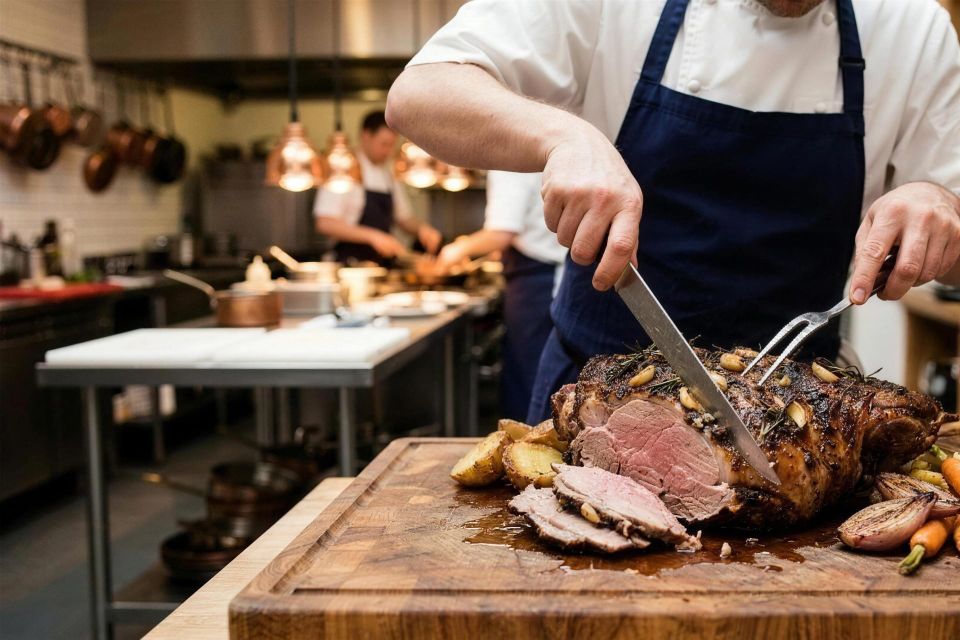 Chef carving a slow roasted shoulder of lamb on a wooden board, roast vegetables and a bowl of dressing alongside.