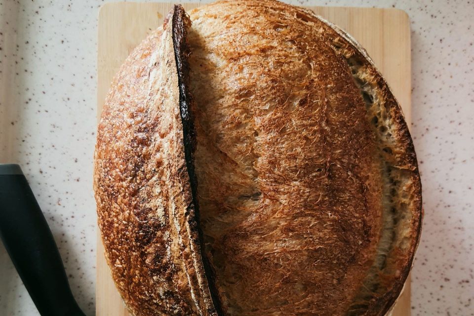 An overhead view of a scored sourdough loaf with a dark, blistered crust, resting on a wooden board