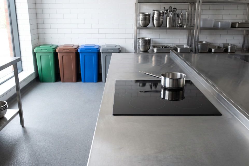 A commercial kitchen with an induction hob and four colour coded waste separation bins lined against the wall