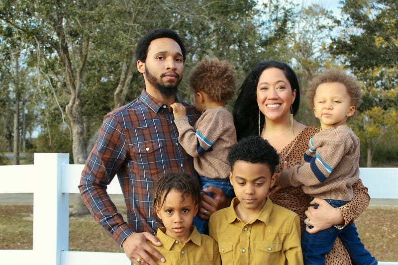 A Black or African-American family (with a father and high-achieving wife / mother) located in Louisiana, Texas, or Washington stands with four (4) children, representing various attachment styles developed in their families of origin.