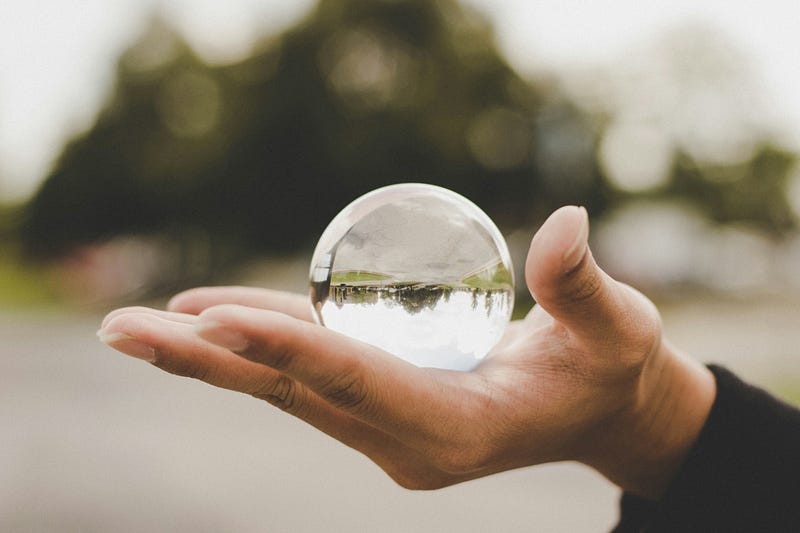 A hand holds a magical crystal ball for fortune-telling or predicting the future. The image is upside down and distorted. It is difficult to see the image clearly, and the background is blurry or fuzzy. This indicates a distorted perspective.