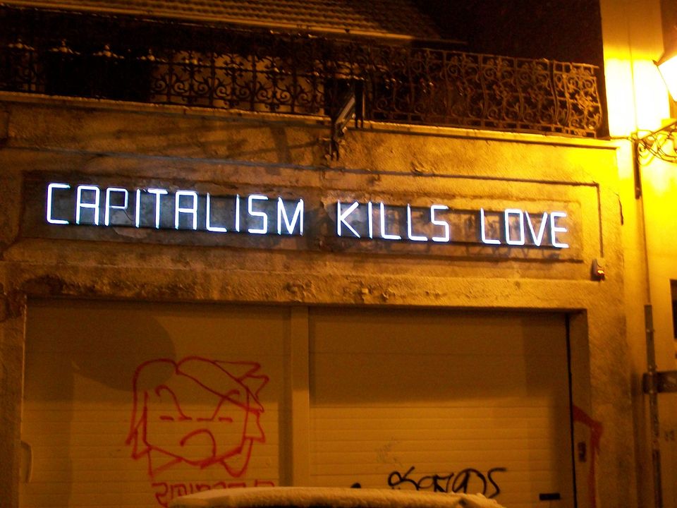 Neon sign that reads capitalism kills love on the street.