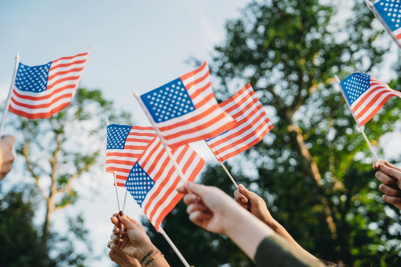 Group holding up American flags. On America's 250th birthday, millions of voters declare their independence. 
