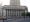 A Classical Revival-style courthouse photographed from across a public square and bollard-lined street. The facade is grey granite.