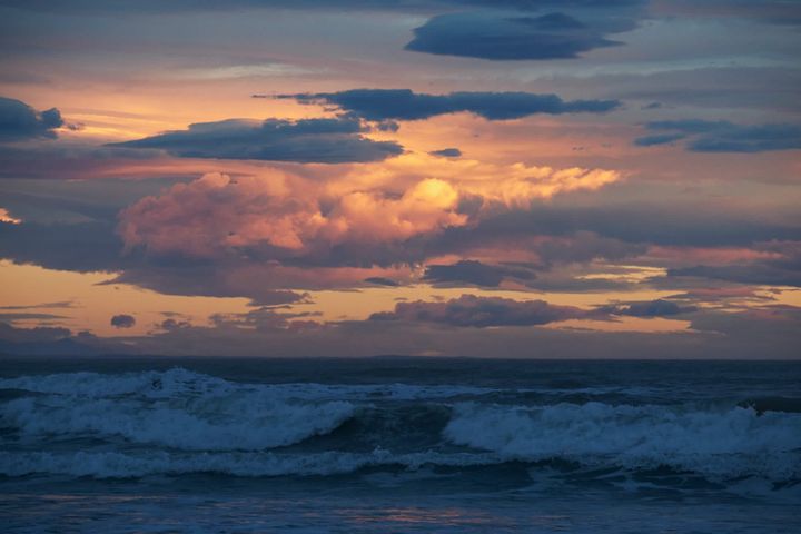 Orange and yellow clouds obscuring the sun and waves crashing on Waimairi Beach, New Zealand. | Photo © 2023 Gary Easterbrook All rights reserved.