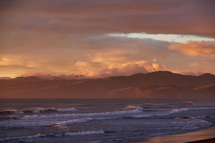 Waves and whitewater on the beach in the forground and Banks Peninsula behind, in orange hues.  Bankl Peninsula,  New Zealand. | Photo © 2023 Gary Easterbrook All rights reserved.
