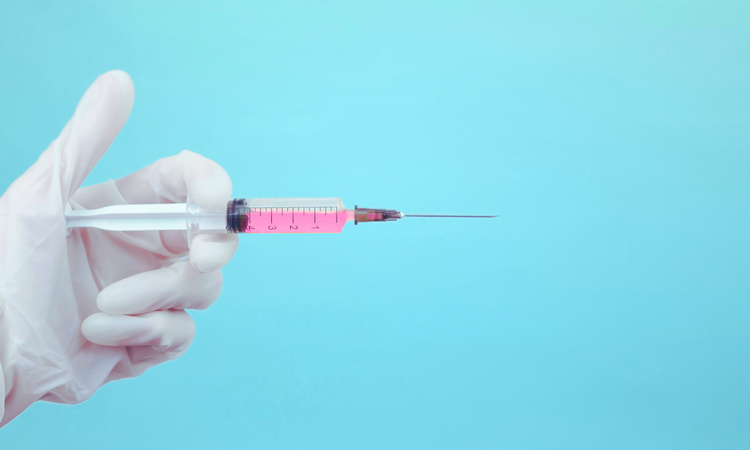 Hand in white latex glove holding a syringe with pink liquid on light blue background.