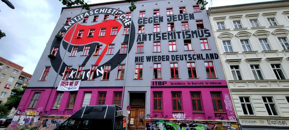 A painted mural on the exterior of an apartment building reads: 'Antifaschistische Aktion - Gegen Jeden Antisemitismus nie wieder Deutschland.'