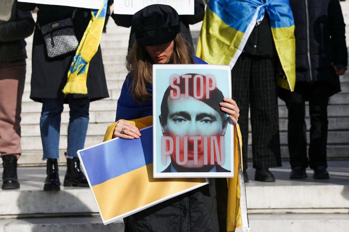 Женщина на демонстрации в поддержку Украины держит в руках плакат с карикатурным изображением Путина