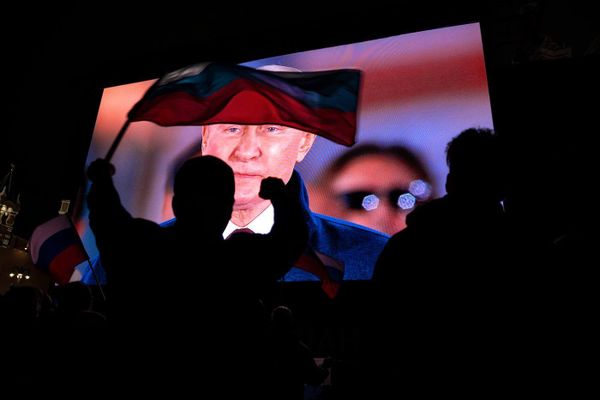 Illustration: Putin on a giant screen in front of Russian citizens, one of which is holding Russian flag. Is Russia fascist?