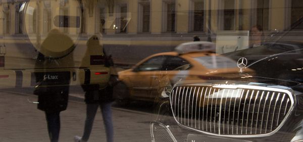 Мерседес, которые теперь импортирует контрабанда, за стеклом витрины, в отражении — улица и люди