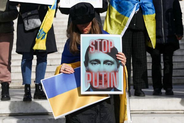 Женщина на демонстрации в поддержку Украины держит в руках плакат с карикатурным изображением Путина