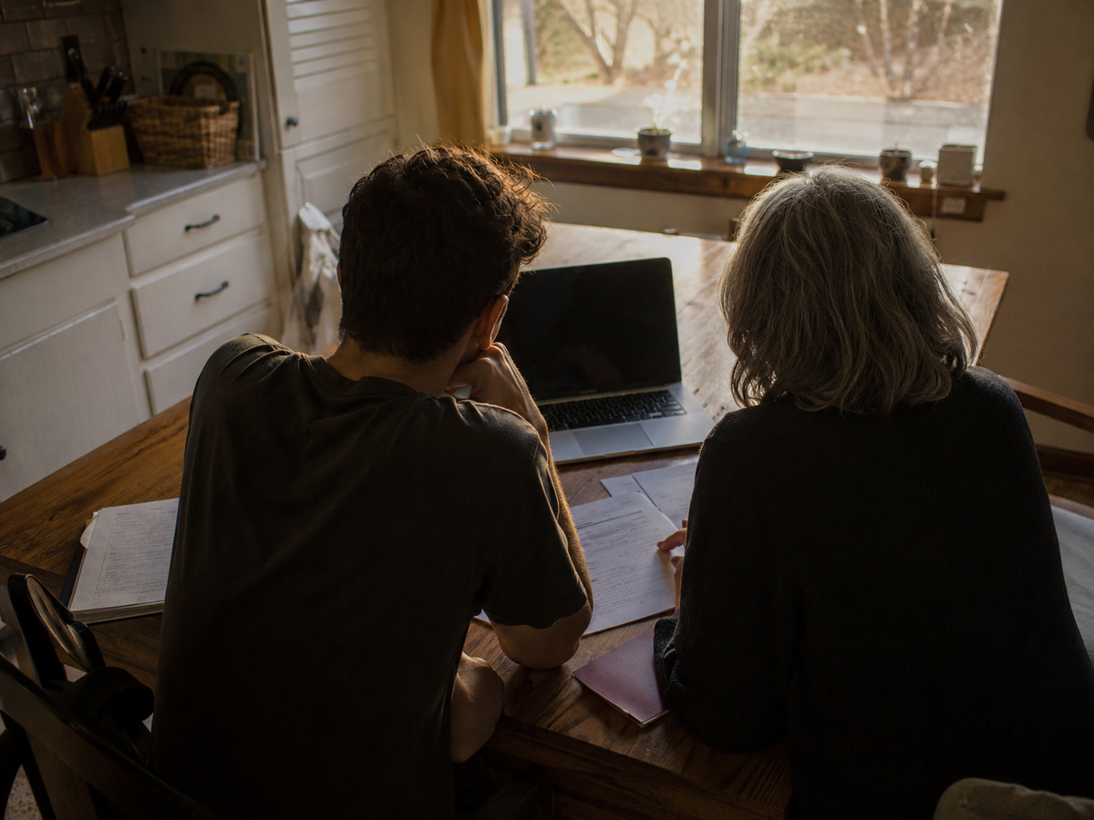 Two people at a kitchen table with a laptop and papers, working through a decision together.