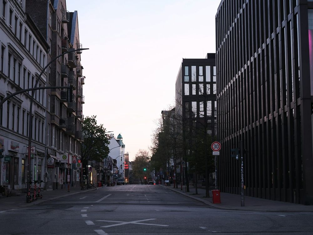 A wide, completely empty city street lined with modern and older buildings in muted neutral tones, photographed in the quiet light before rush hour.