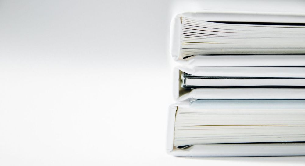A neat stack of thick white document folders filled with paper reports rests on a plain white surface, minimal and unbranded.