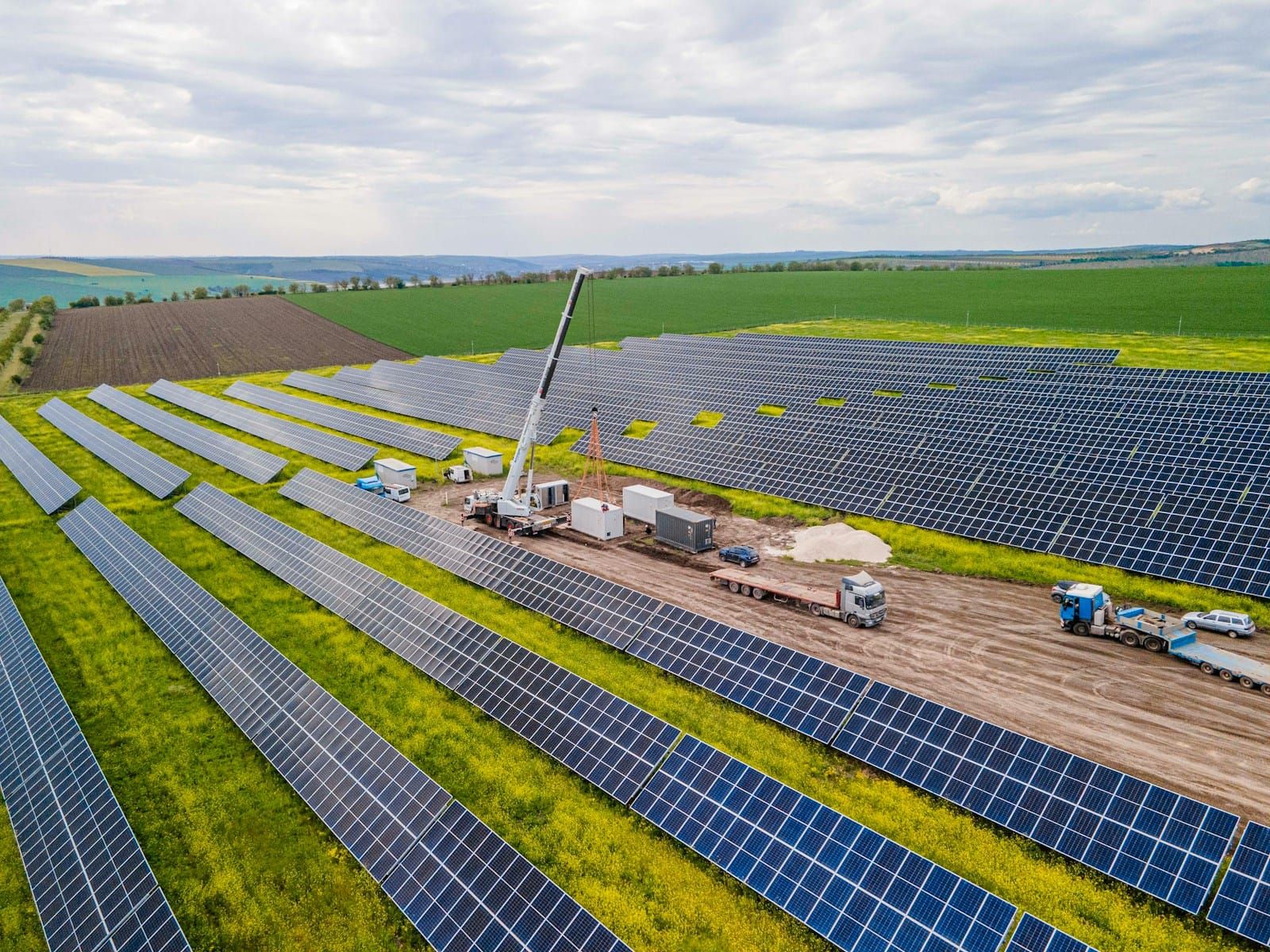 Aerial view of a solar panel field under construction, with a crane working among the rows of panels.