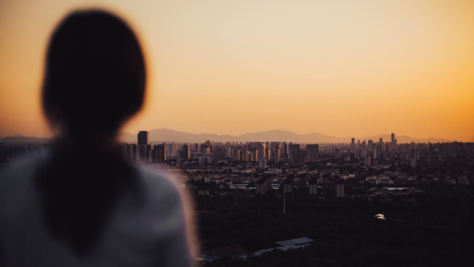 A solitary figure silhouetted against an urban skyline at dusk as the city fades into golden light.
