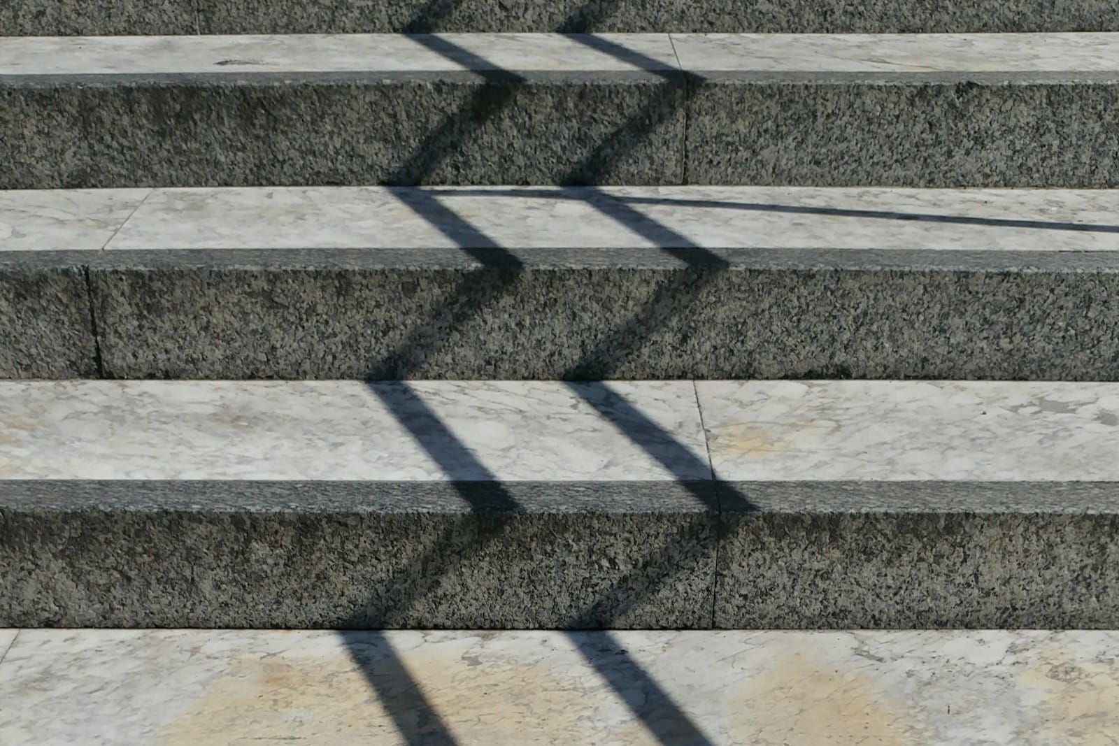 Grey and white concrete steps with hard zigzag shadows, an abstract stepped pattern resembling a rising step chart.