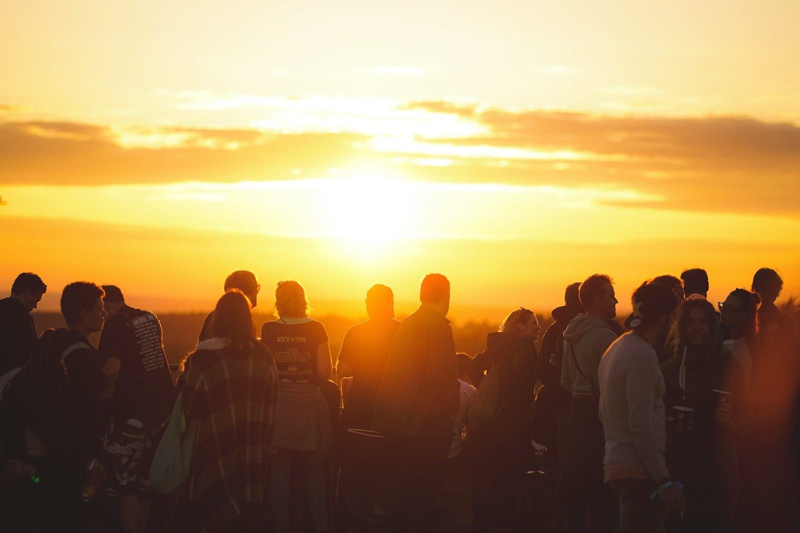 A large outdoor crowd of young people silhouetted from behind against a golden sunset sky.