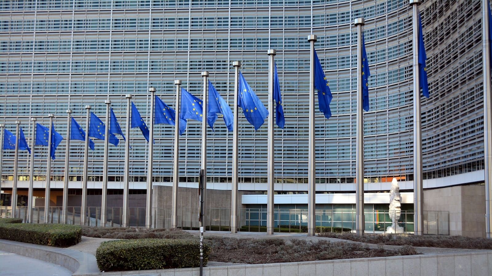 Rows of blue European Union flags on poles outside the Berlaymont building in Brussels.