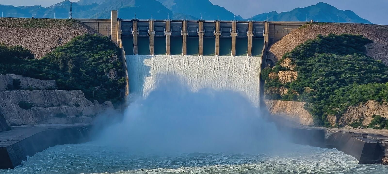 A large concrete hydroelectric dam with water cascading through its open spillways.