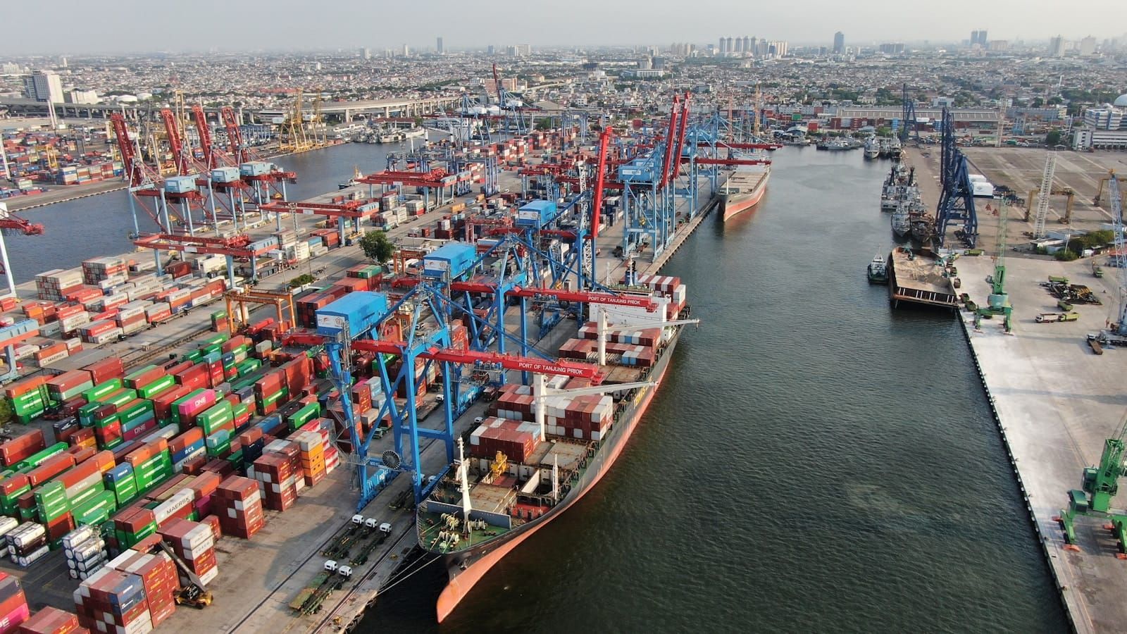 Aerial view of a busy container port with gantry cranes loading stacked shipping containers.
