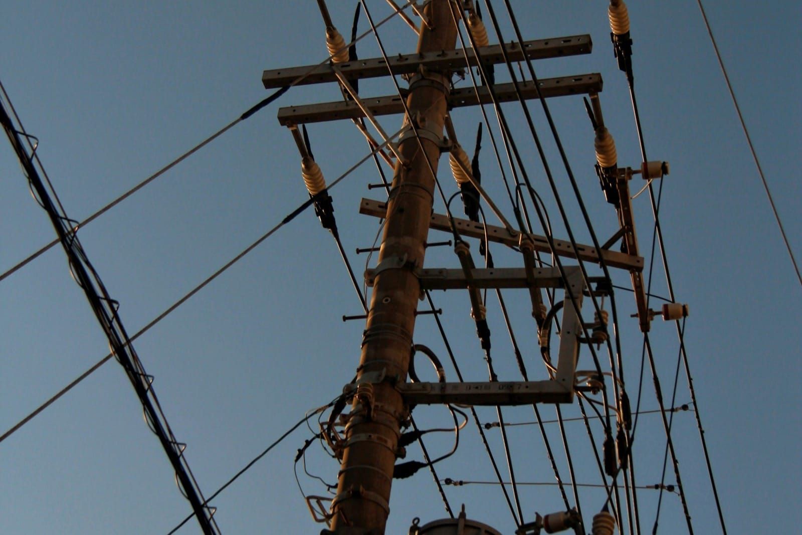 A single wooden utility pole with a transformer and low-voltage service wires photographed against a plain pale sky.