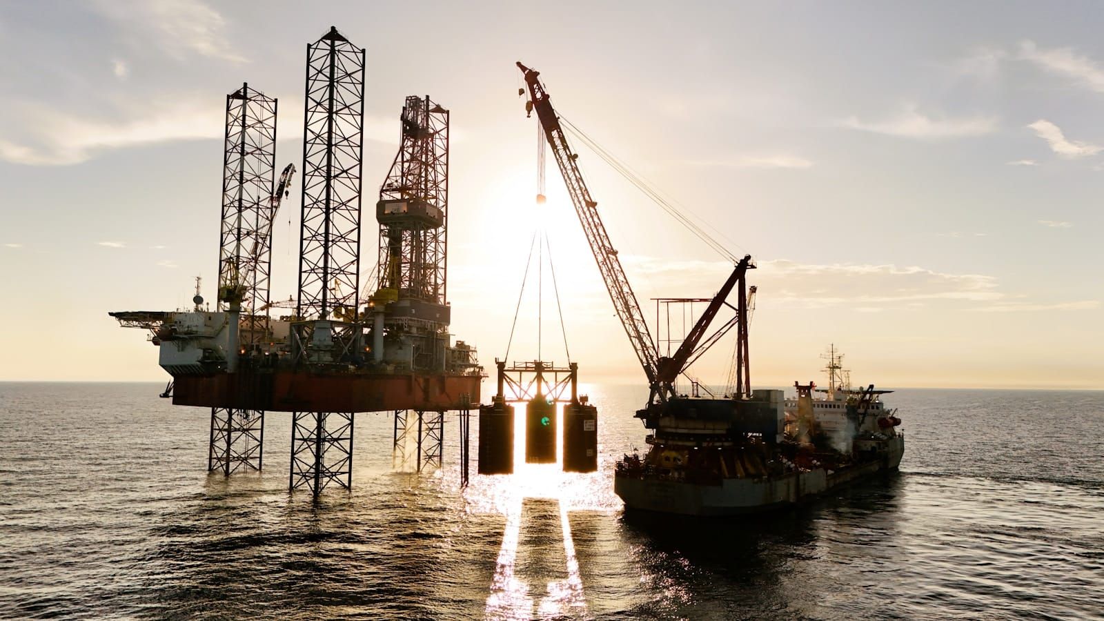 An offshore oil platform at sea being serviced by a supply vessel alongside.