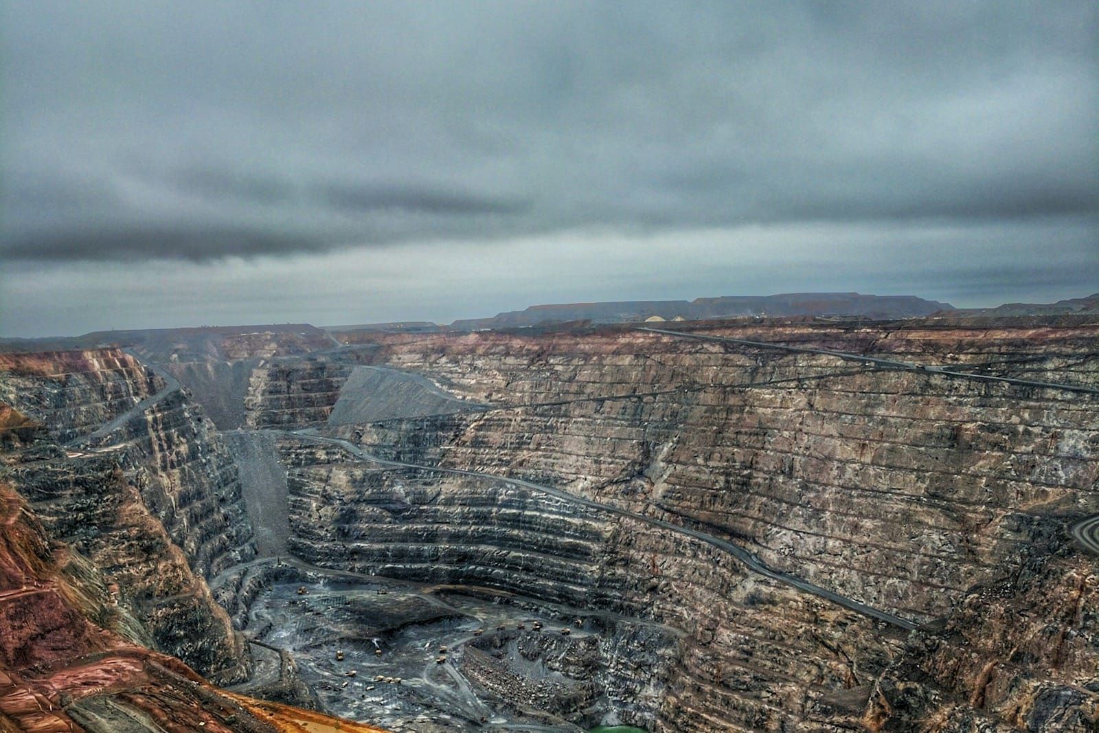 A vast open-pit mine seen from above, with mining trucks working the terraced valley floor.