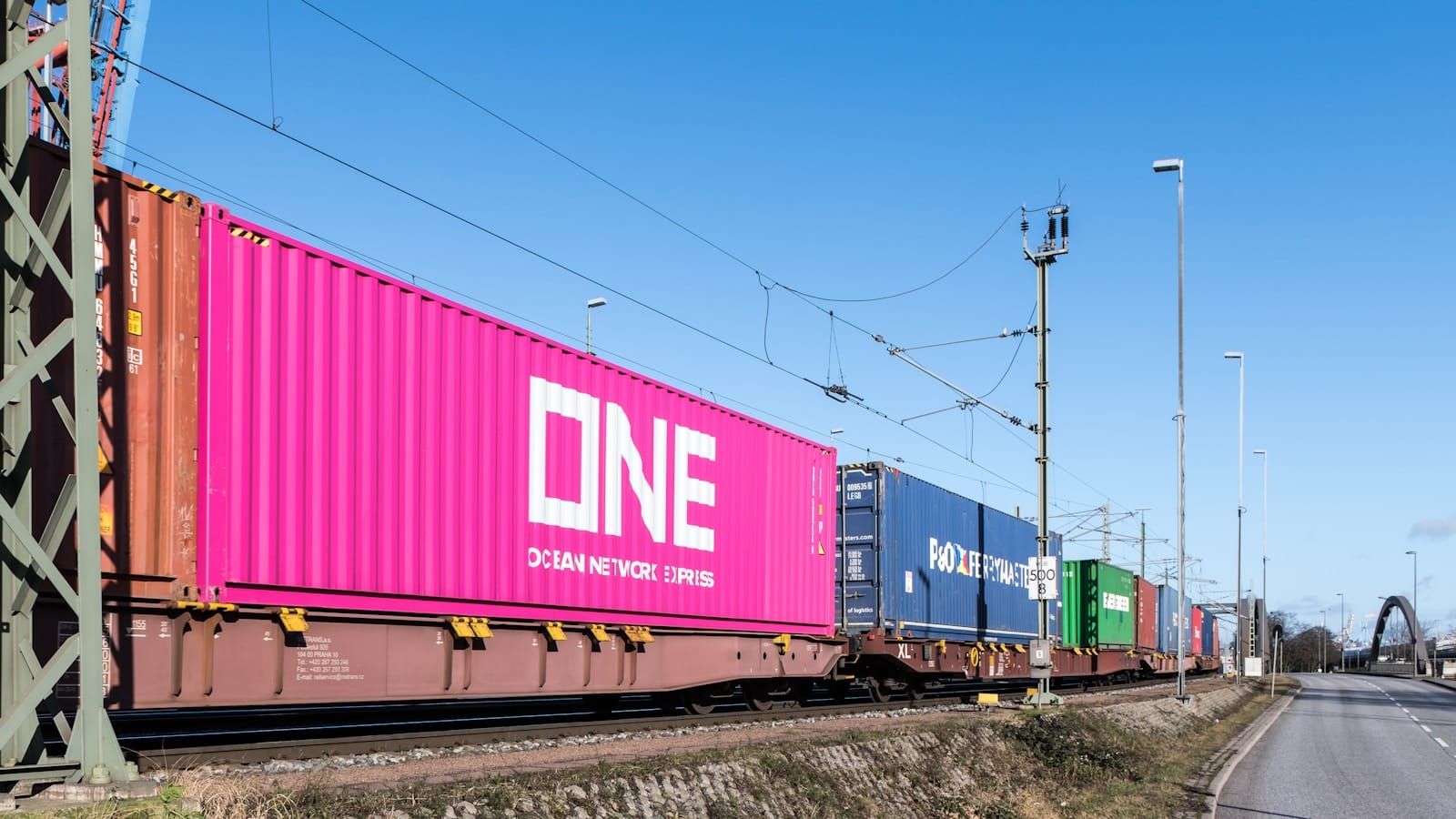 A freight train carrying shipping containers along rail tracks with an urban skyline behind, in Hamburg.