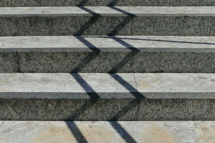Grey and white concrete steps with hard zigzag shadows, an abstract stepped pattern resembling a rising step chart.