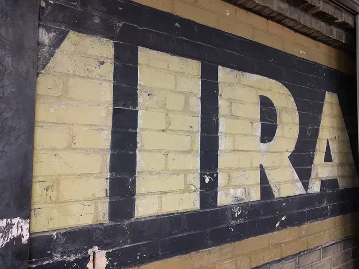 A brick wall with a faded sign and partial letters: M, I, R, A.
