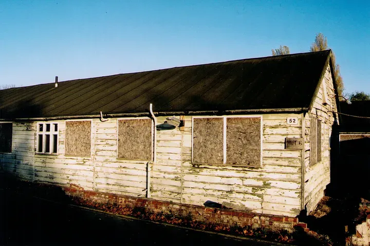 A run down wooden building with boarded-over windows and peeling white paint.
