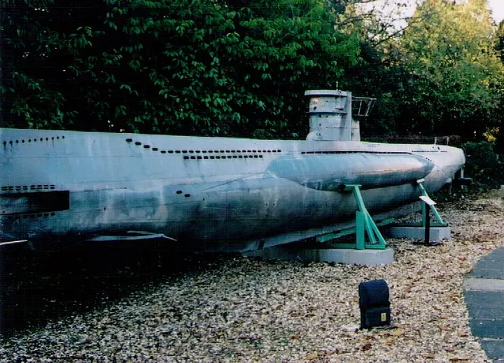 A replica of a German u-boat mounted on concrete pads in front of a hedge.